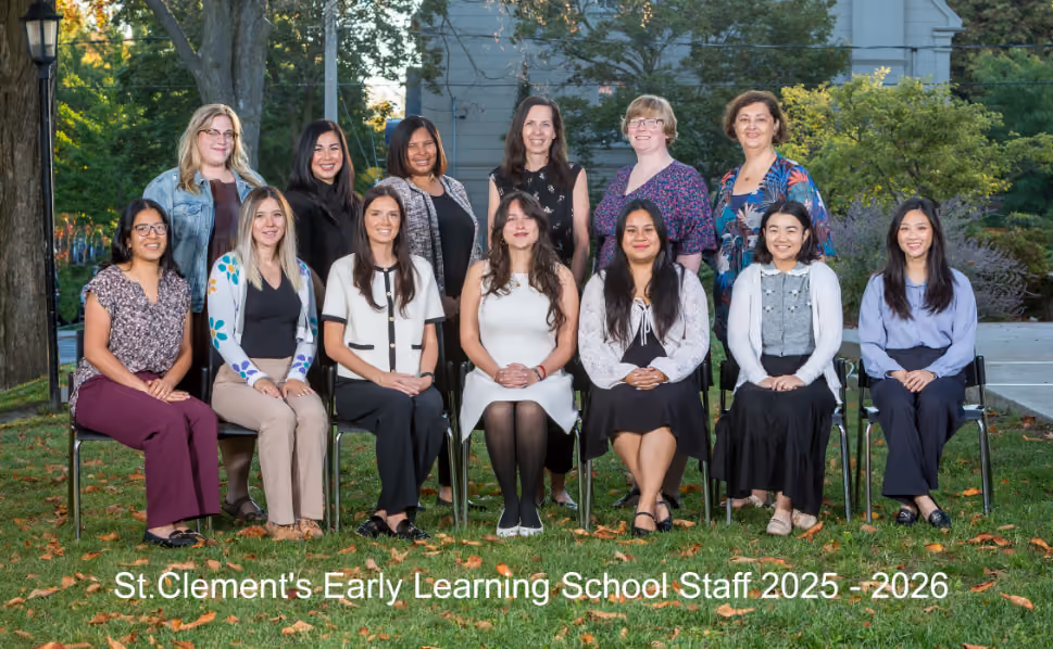 Group photo of 13 female staff members of St. Clement's Early Learning School posing outdoors on grass with trees and a building in the background, labeled 2025-2026.