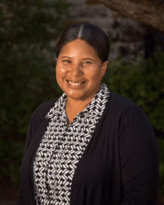 Smiling woman with dark hair parted in the middle, wearing a black and white patterned blouse and black cardigan.