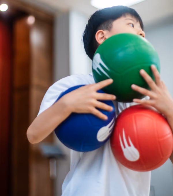Young boy holding three colorful balls—green, blue, and red.