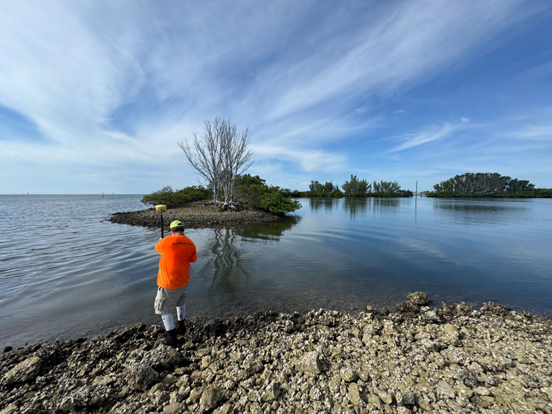 A Davris surveyor is collecting shoreline and coastal GPS data along a rocky Florida waterfront during a marine surveying project.