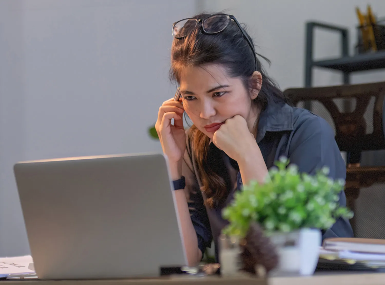 Woman with glasses on her head looking intently at a laptop screen while resting her chin on her hand.
