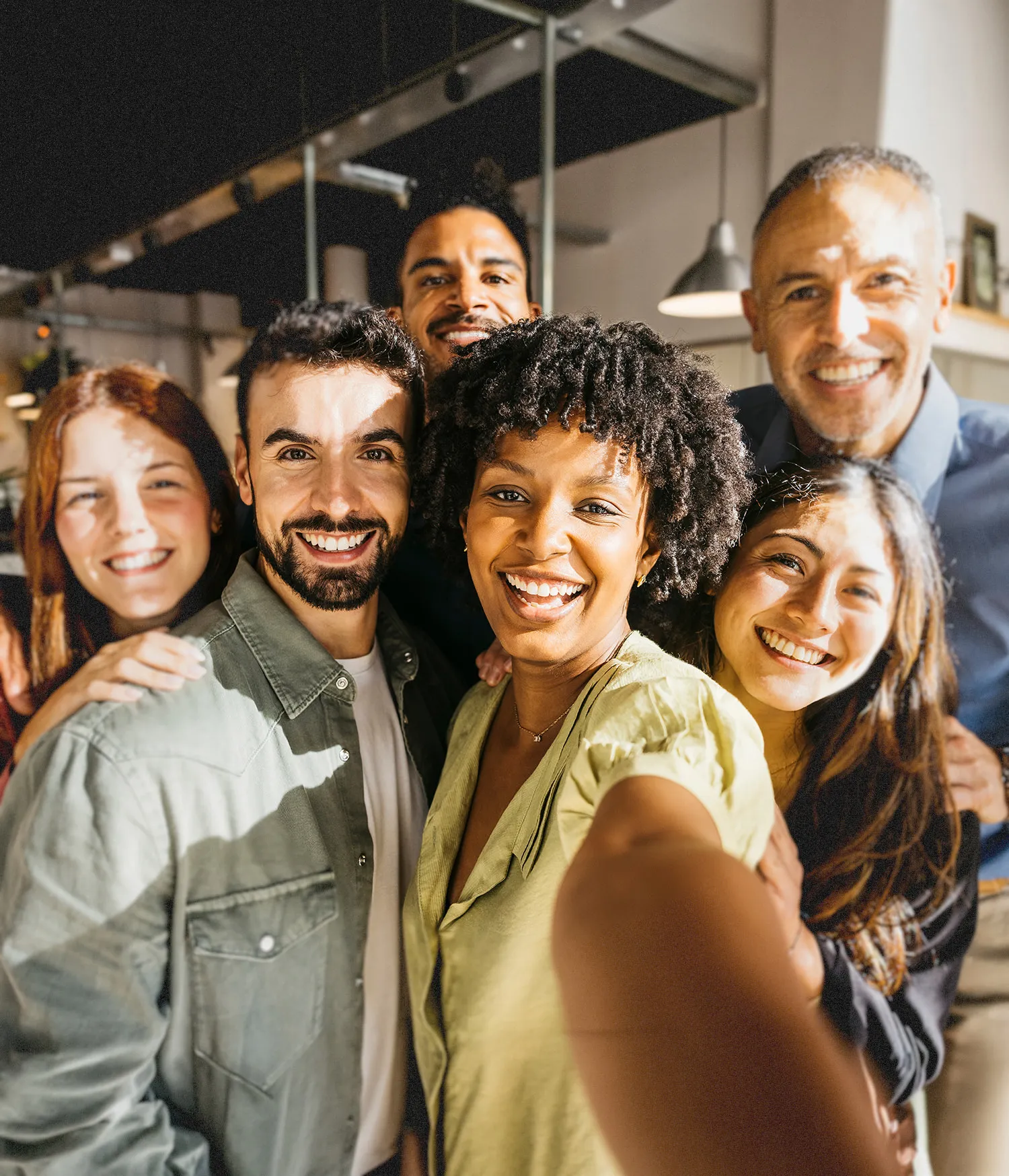 Group of six diverse young adults smiling together for a selfie indoors.