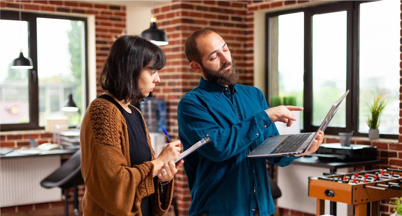 Woman with blonde hair in a striped shirt sitting at a white desk, holding a pen and looking to the side with a laptop and mug nearby.