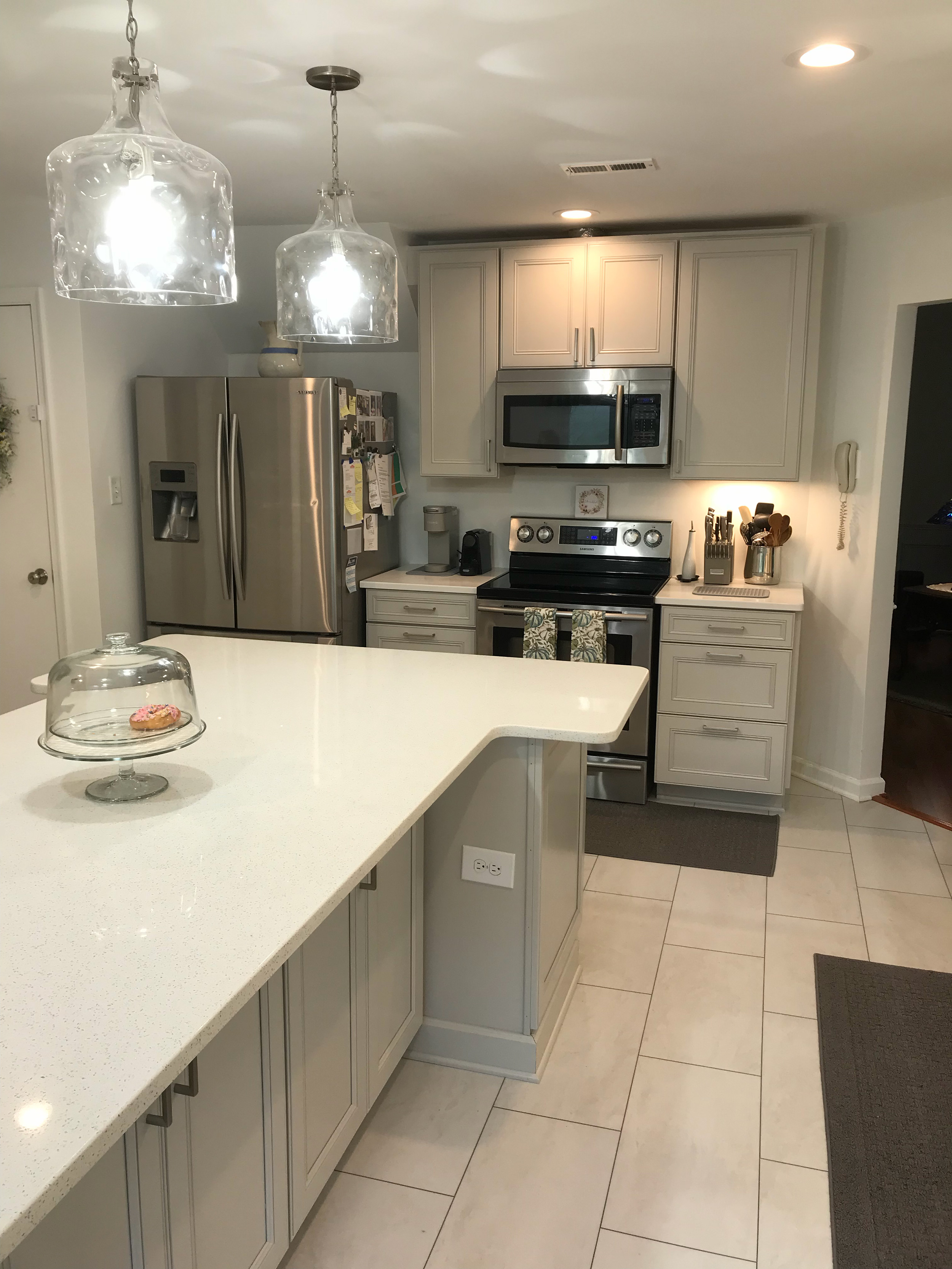 Modern kitchen renovation with an oversized white island, pendant lights, and stainless steel appliances.
