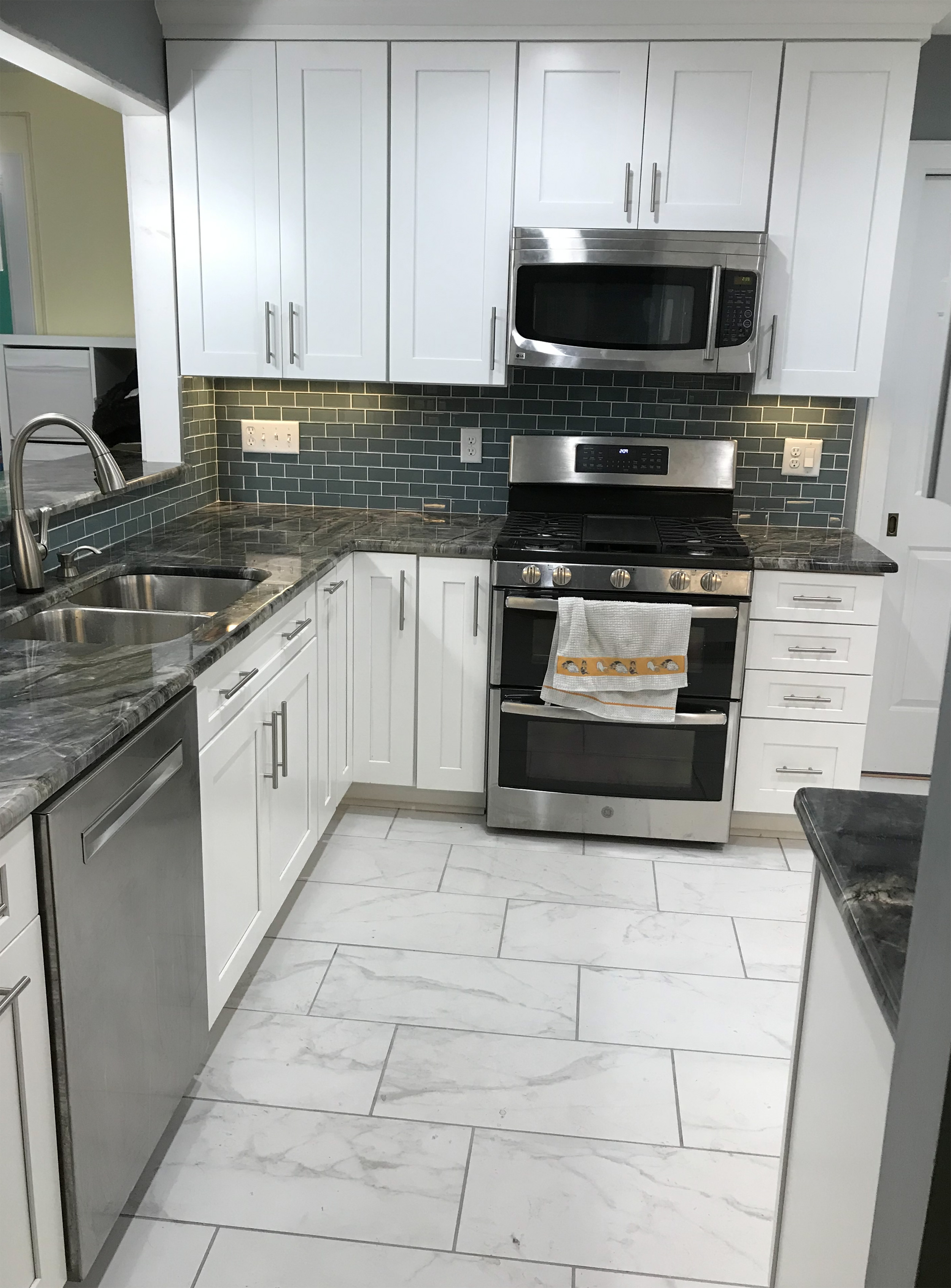 White galley kitchen with granite countertops, tile flooring, and stainless steel appliances.