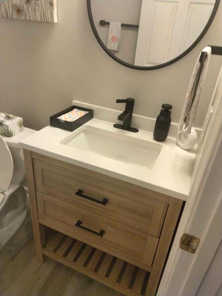 Wood bathroom vanity with a white countertop, black fixtures, and round mirror.