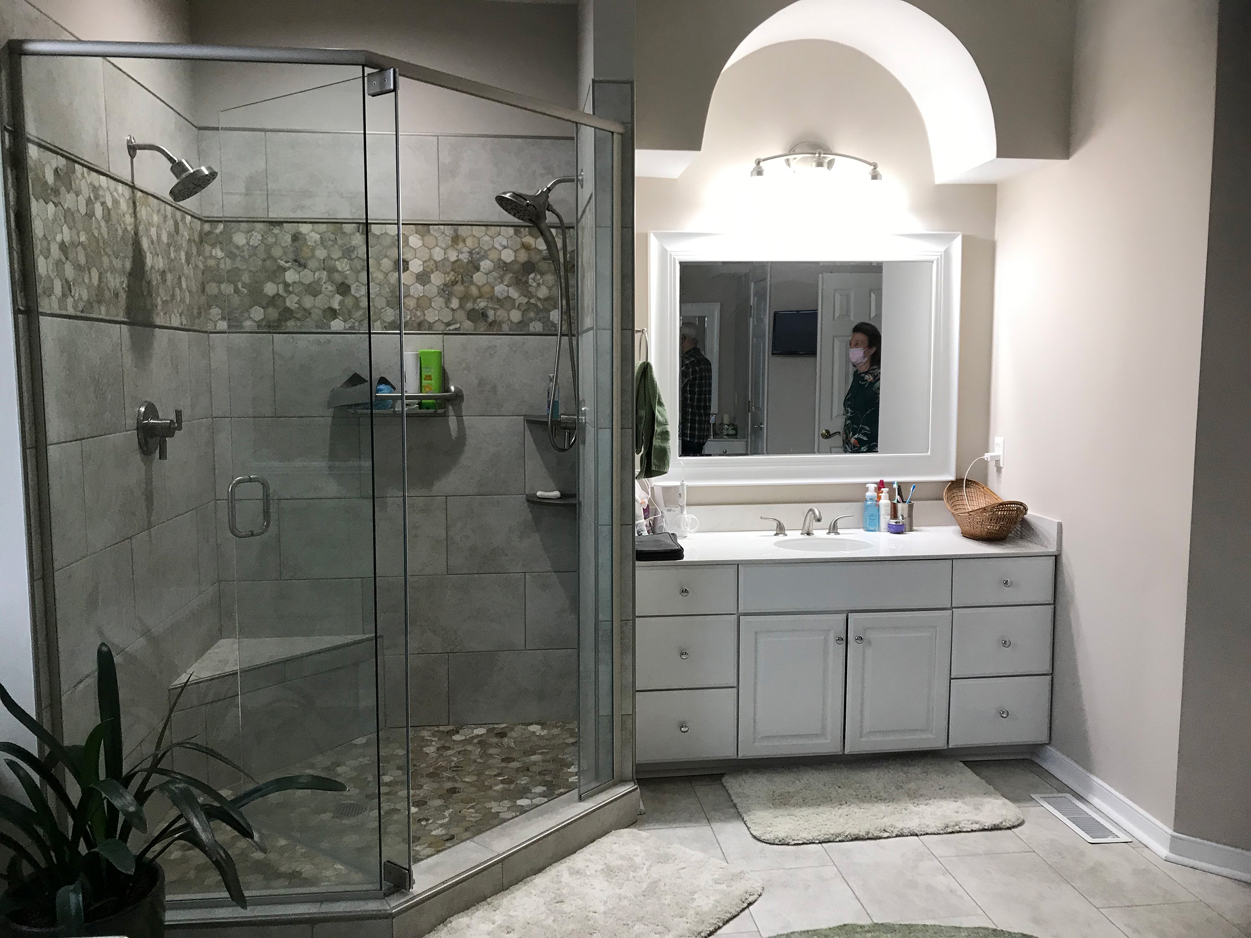 Remodeled bathroom with a glass walk-in shower, double vanity, and arched mirror.