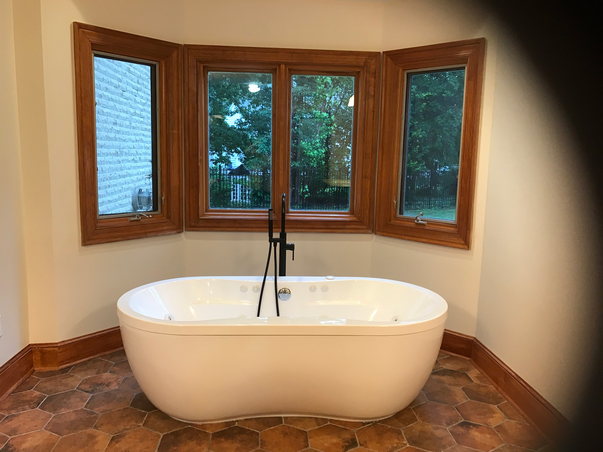 Freestanding soaking tub beneath wood-trimmed bay windows.