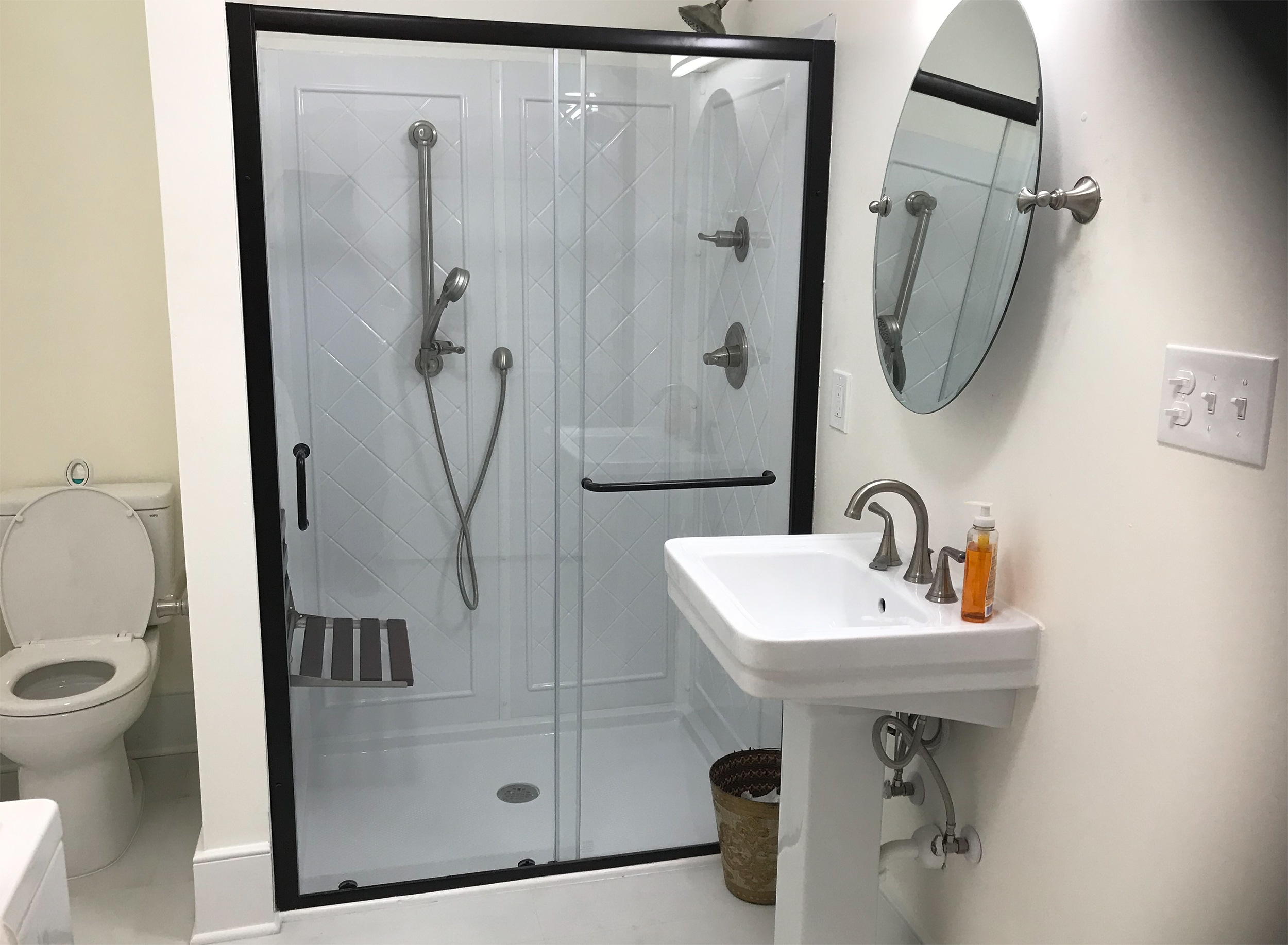 Compact bathroom with a glass shower enclosure, pedestal sink, and round mirror.