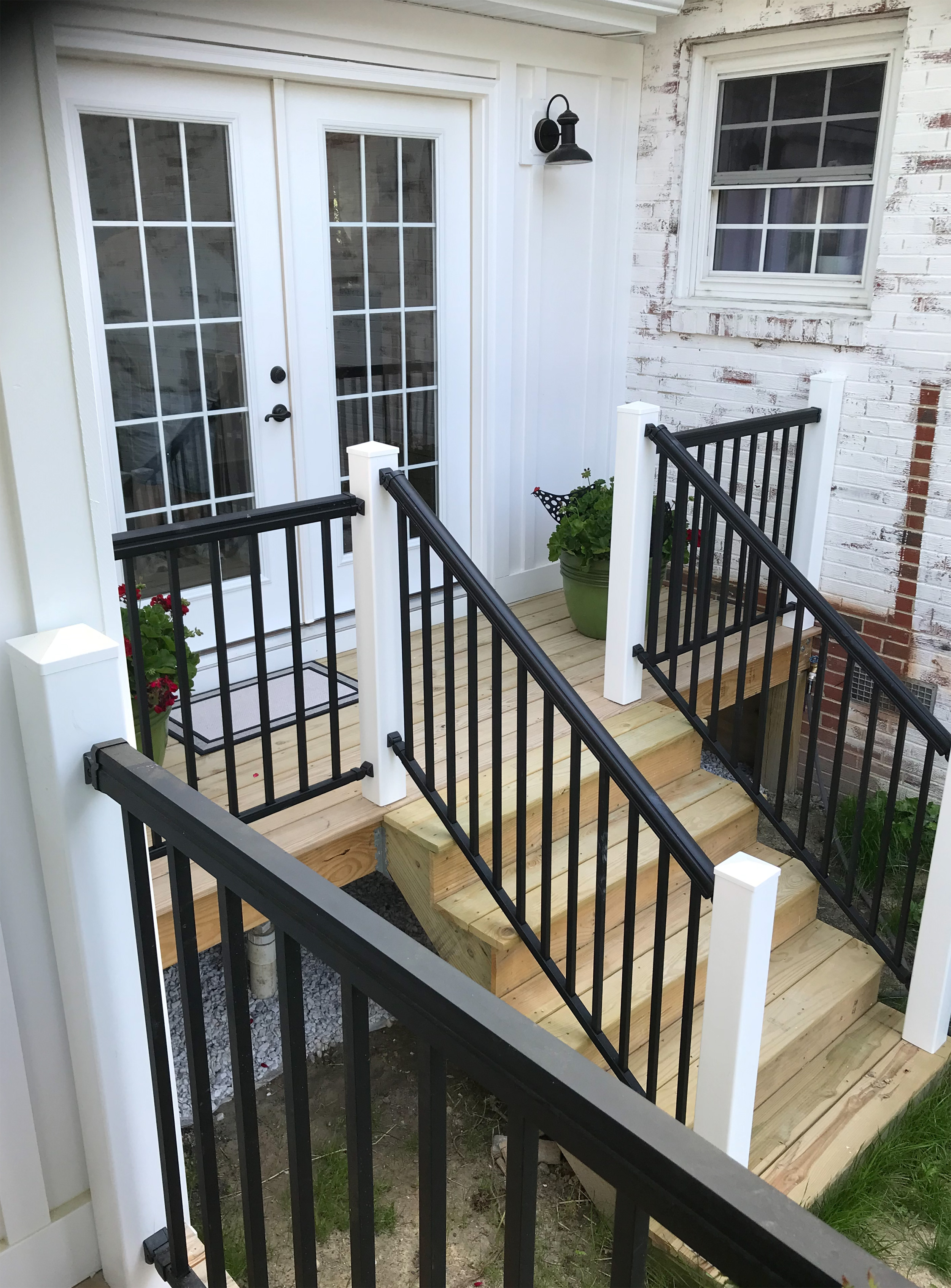 Small exterior landing with white posts, black railings, and wooden steps.