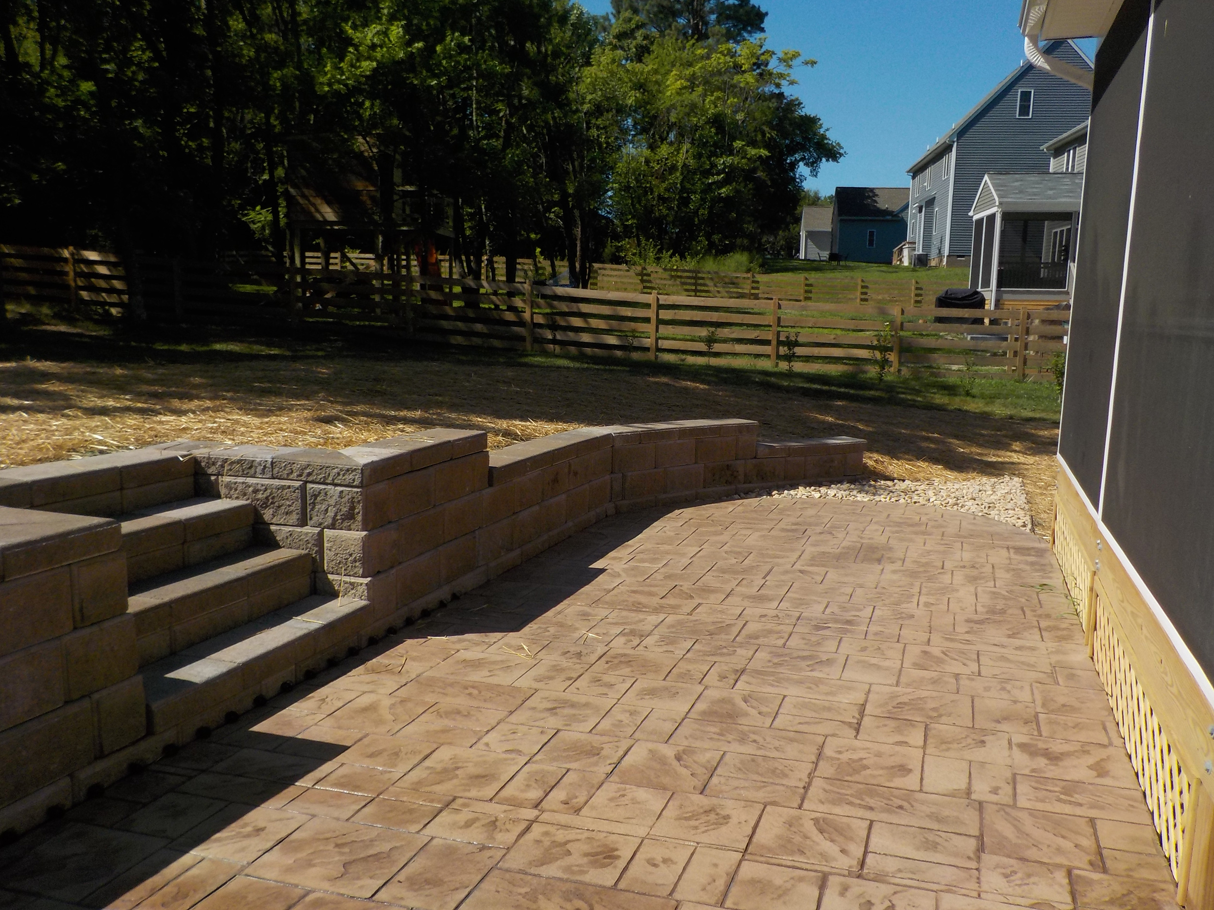 Stamped concrete patio with steps and a block retaining wall beside a home.