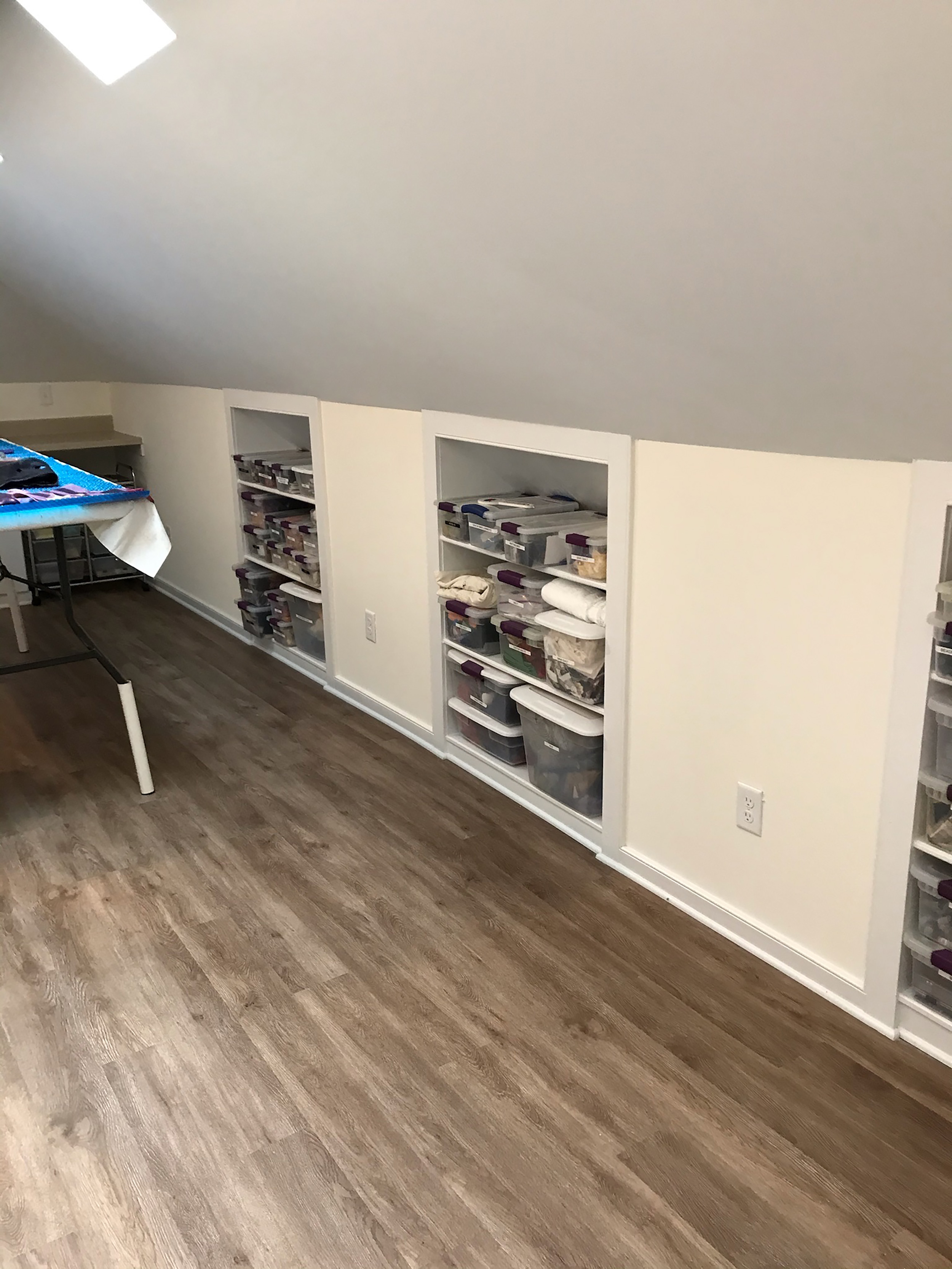 Finished attic room with a sloped ceiling, built-in shelving, and wood-look flooring.