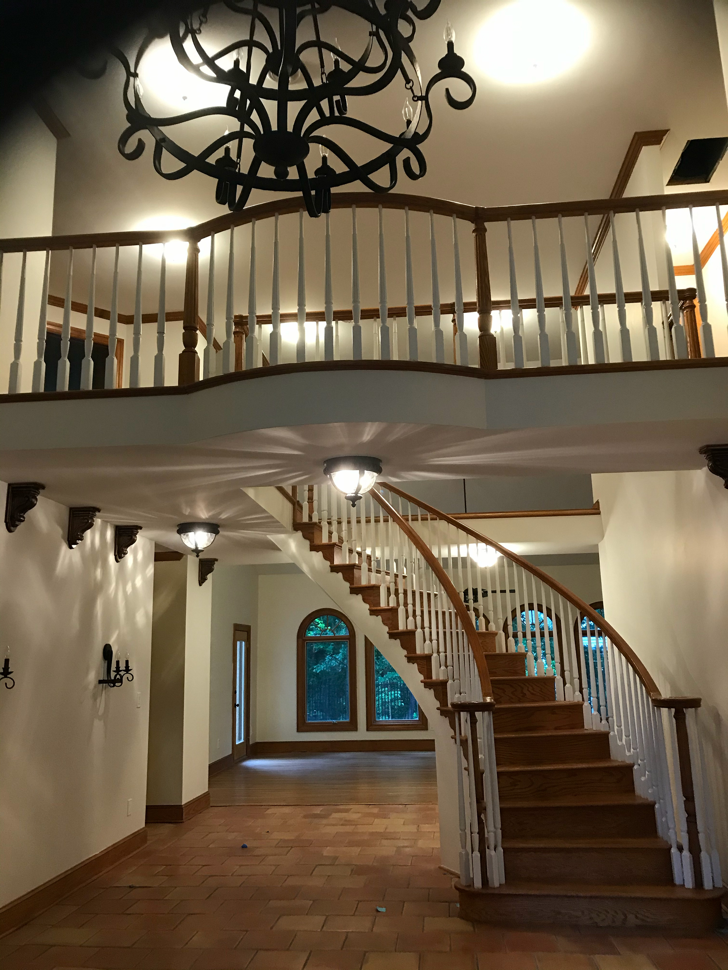 Curved wood staircase with an upper-level balcony railing and decorative chandelier.