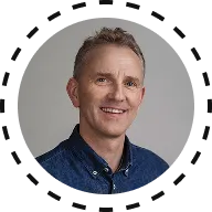 Smiling middle-aged man with short gray hair wearing a blue collared shirt against a gray background.