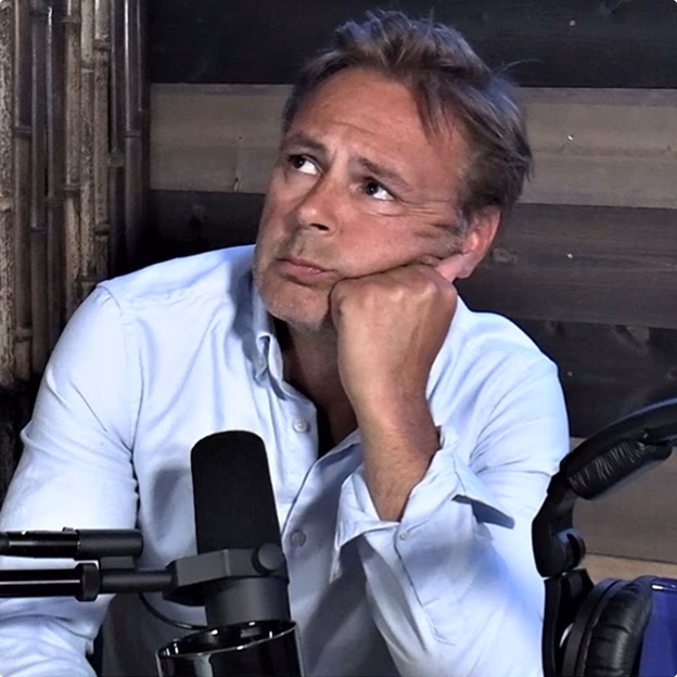 Smiling middle-aged man wearing a dark coat in a warmly lit indoor setting.