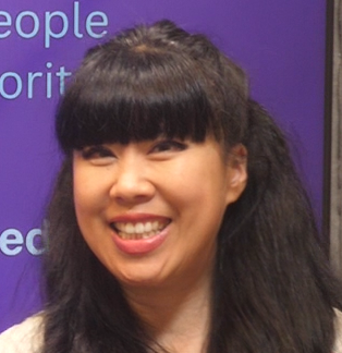 Smiling woman with long black hair and bangs against a purple background with partial text.