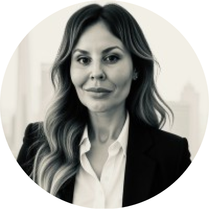 Professional woman with long wavy hair wearing a white blouse and black blazer in a blurred office setting.