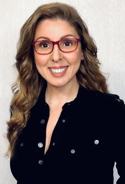 Smiling woman with long wavy hair wearing red glasses and a black buttoned top.