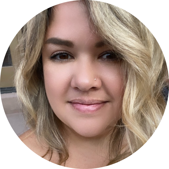 Close-up of a woman with blonde wavy hair, light skin, and a small nose stud, smiling softly.
