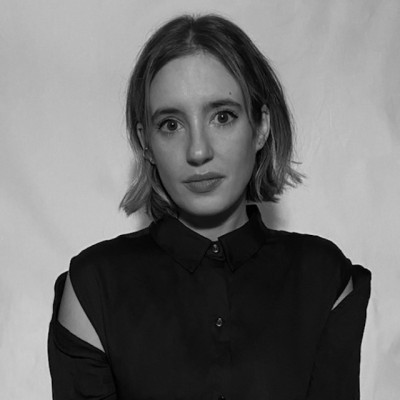 Black and white portrait of a woman with short hair wearing a black shirt with cut-out shoulders against a plain backdrop.