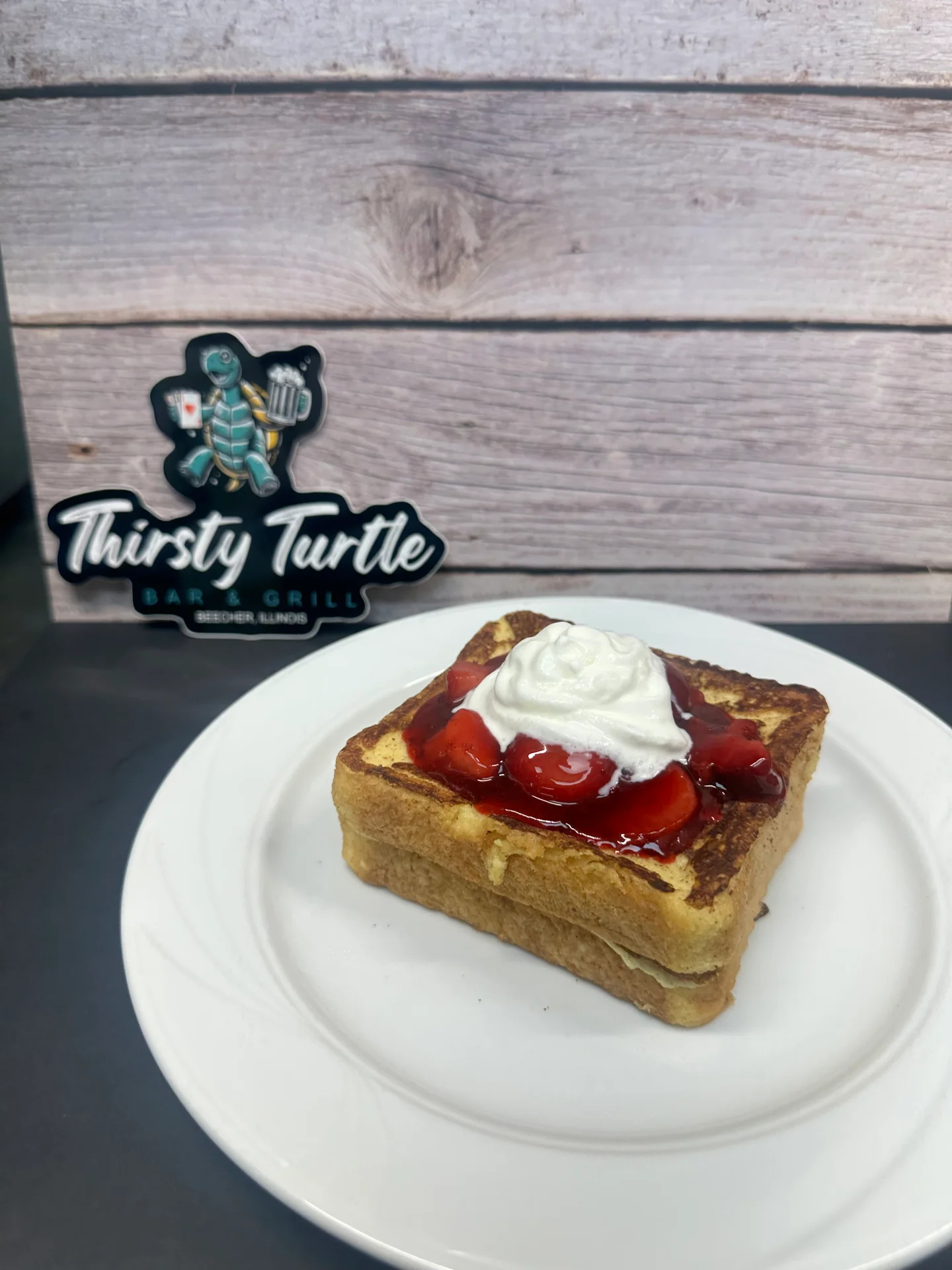 Square serving of French toast topped with strawberry sauce and whipped cream on a white plate.
