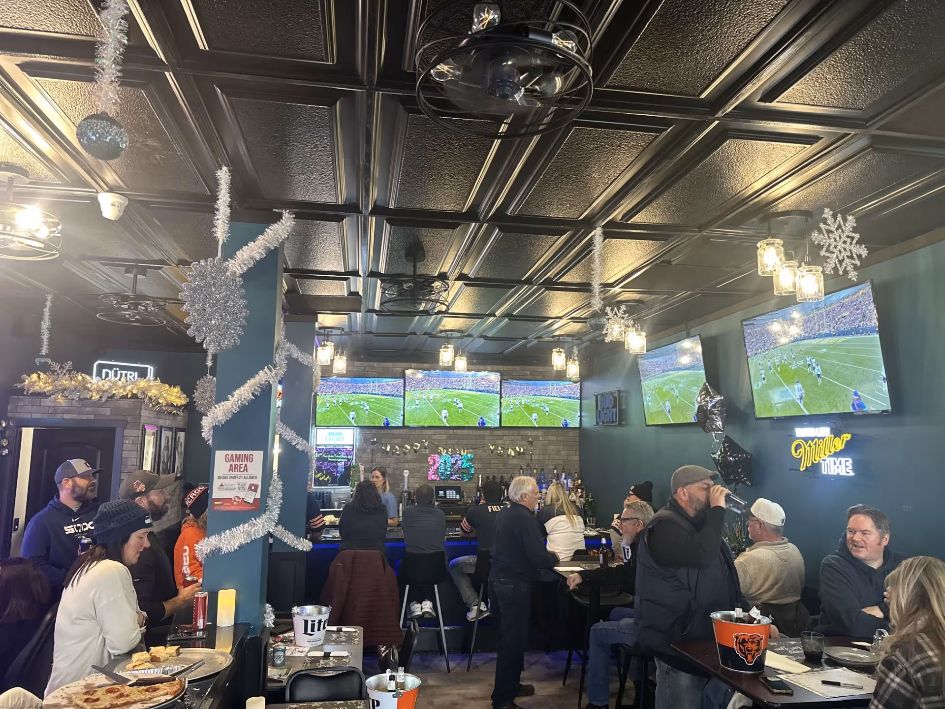 Indoor bar with patrons watching football on multiple TVs, decorated with silver tinsel and snowflakes for the holidays.