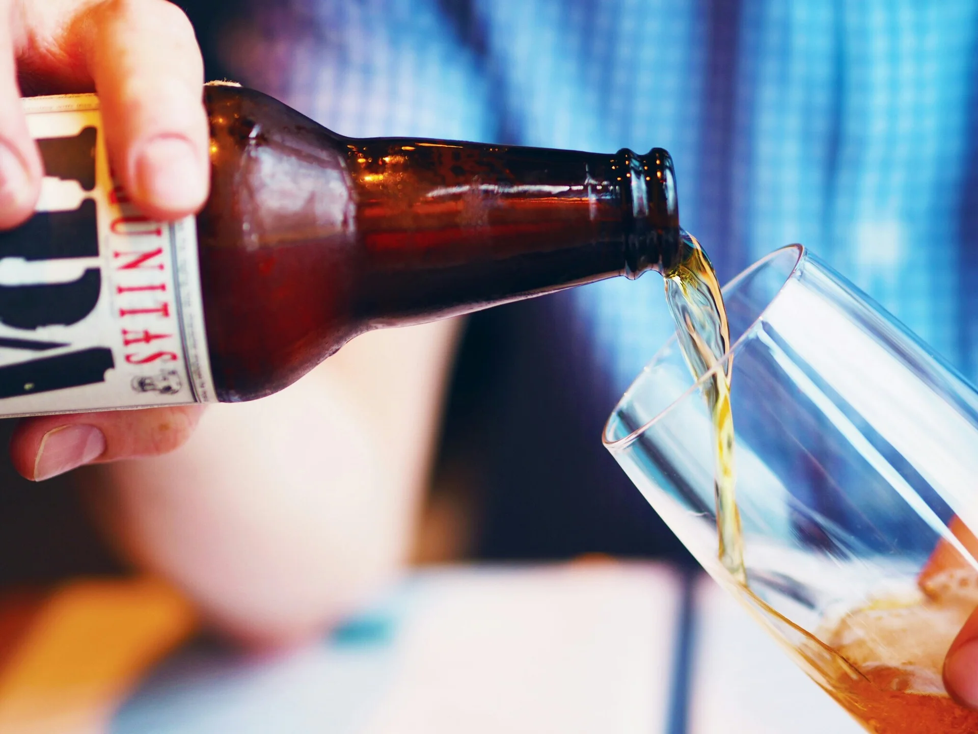 Hand pouring beer from a brown bottle into a tilted glass.