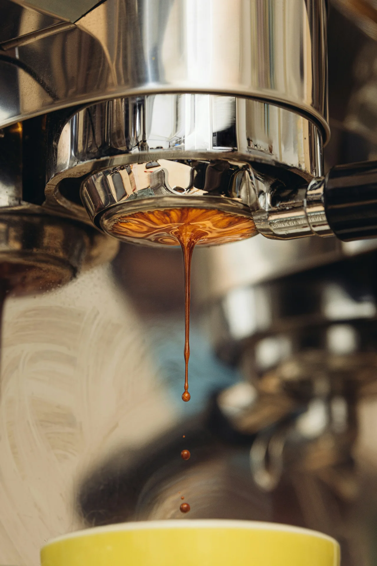 Close-up of espresso dripping from a metal portafilter into a yellow cup.