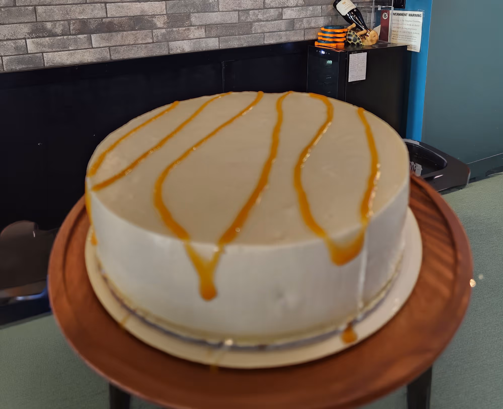 Round white cheesecake with caramel drizzle on top placed on a wooden cake stand.