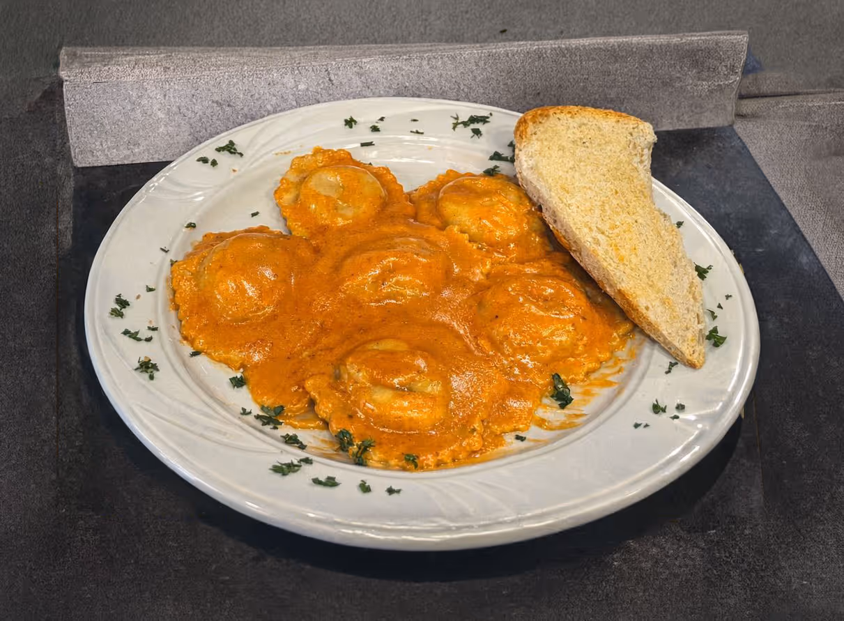 Plate of five ravioli in creamy tomato sauce, garnished with chopped herbs, served with a triangular slice of toasted bread.
