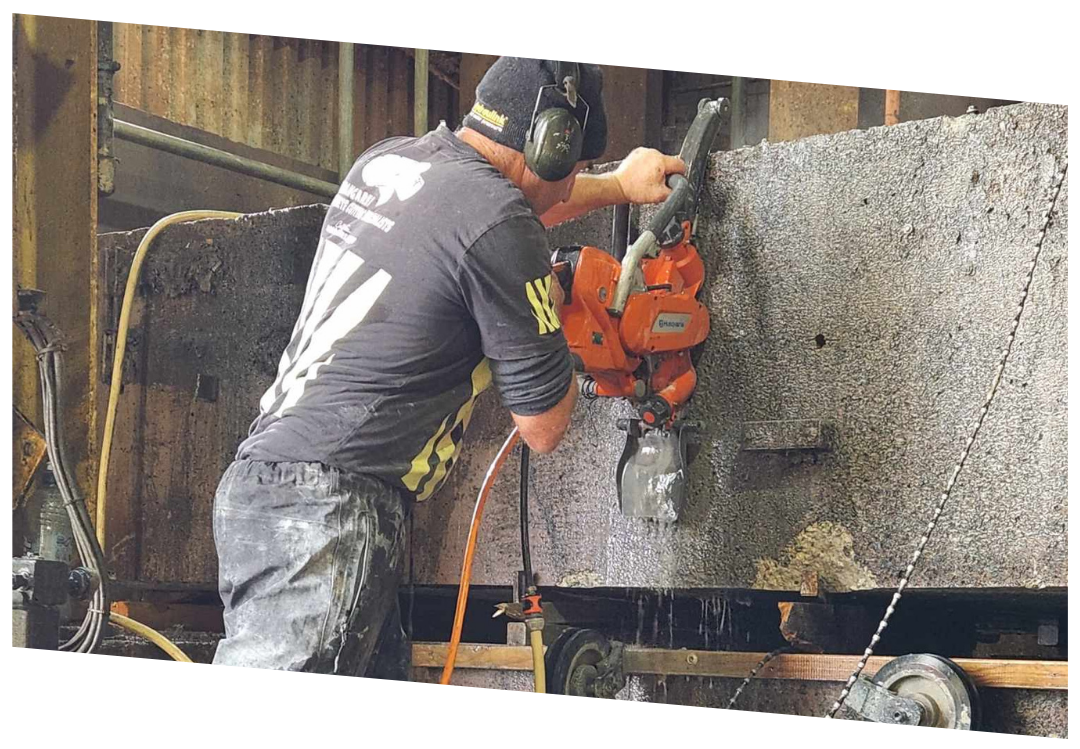 Worker using a large orange stone-cutting machine to saw through a thick block of stone.
