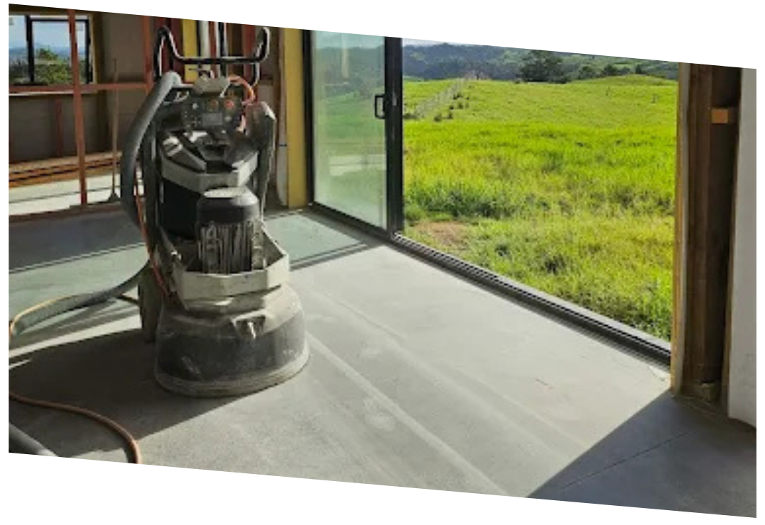Concrete floor grinder machine inside a room with large sliding glass doors overlooking a green field.