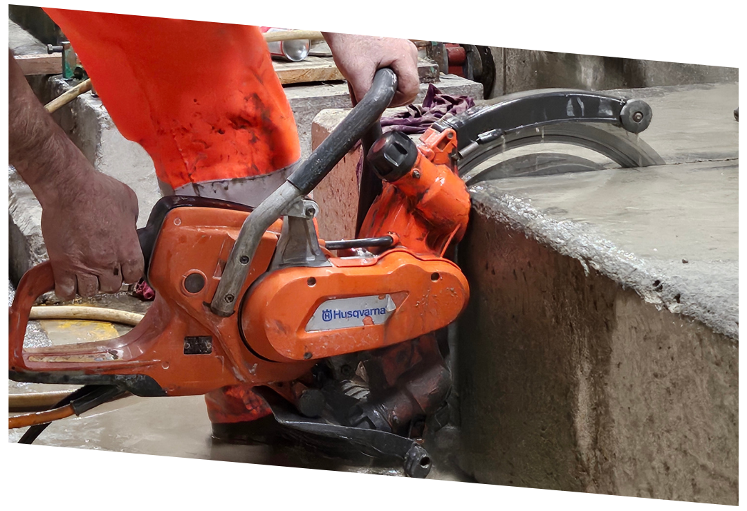 Construction worker cutting concrete with orange Husqvarna power saw.