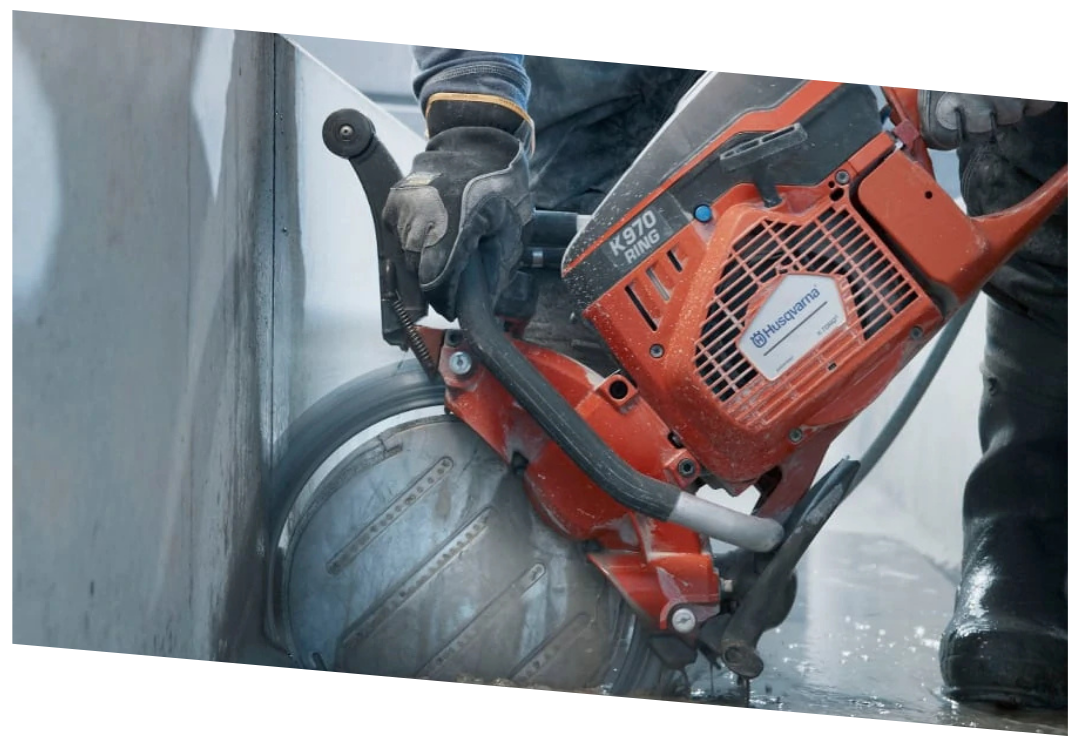 Worker using a Husqvarna K970 Ring power saw to cut concrete near a wall.