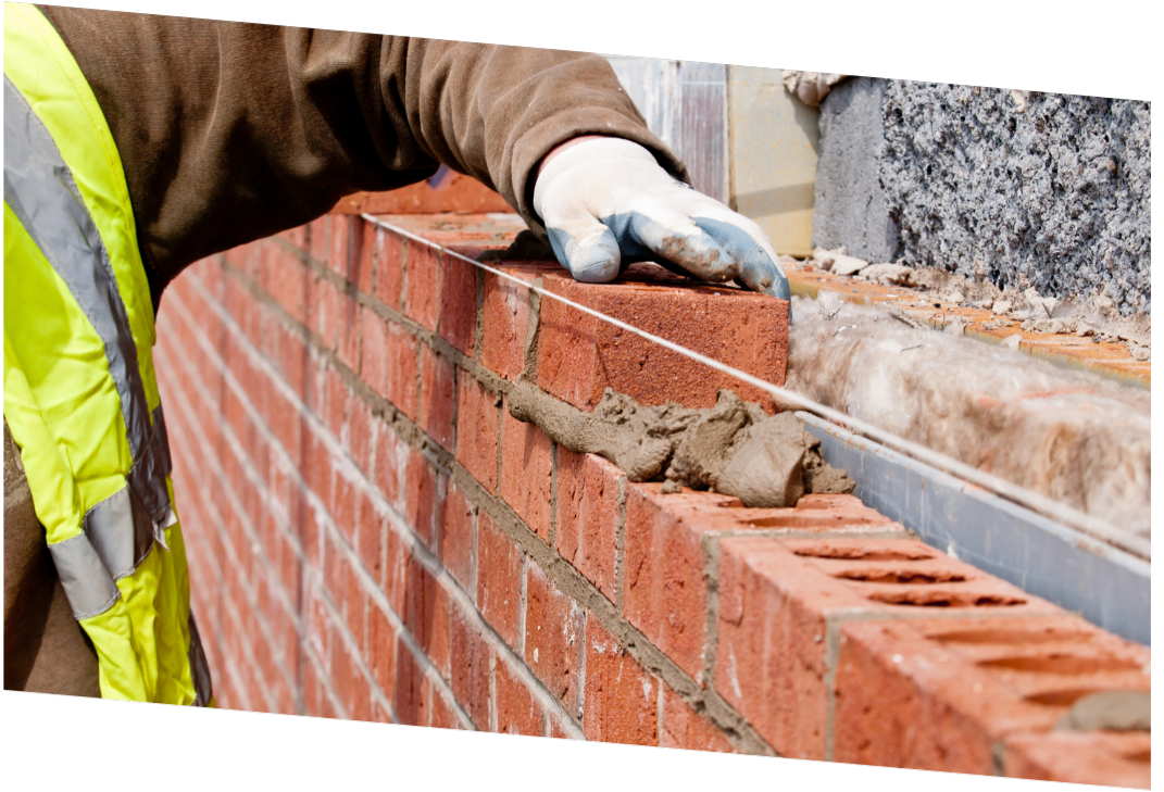 Construction worker in yellow vest laying red bricks with cement on a wall.