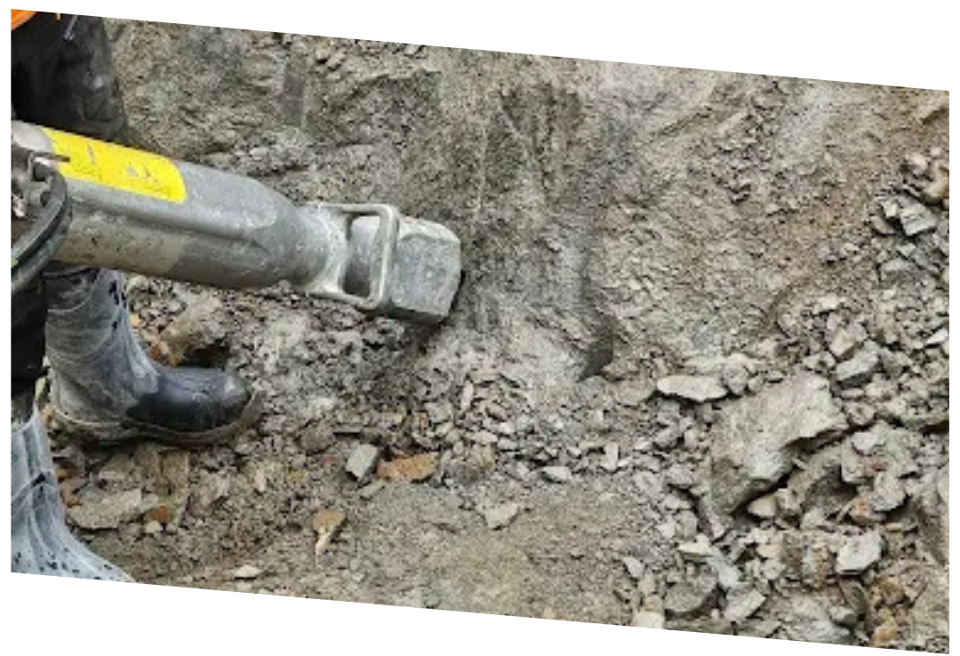 Close-up of a jackhammer breaking rocky ground at a construction site.