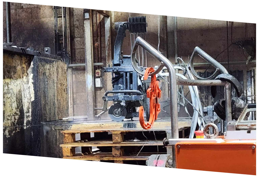 Industrial machine with metal frame and orange clamps in a dimly lit factory setting.