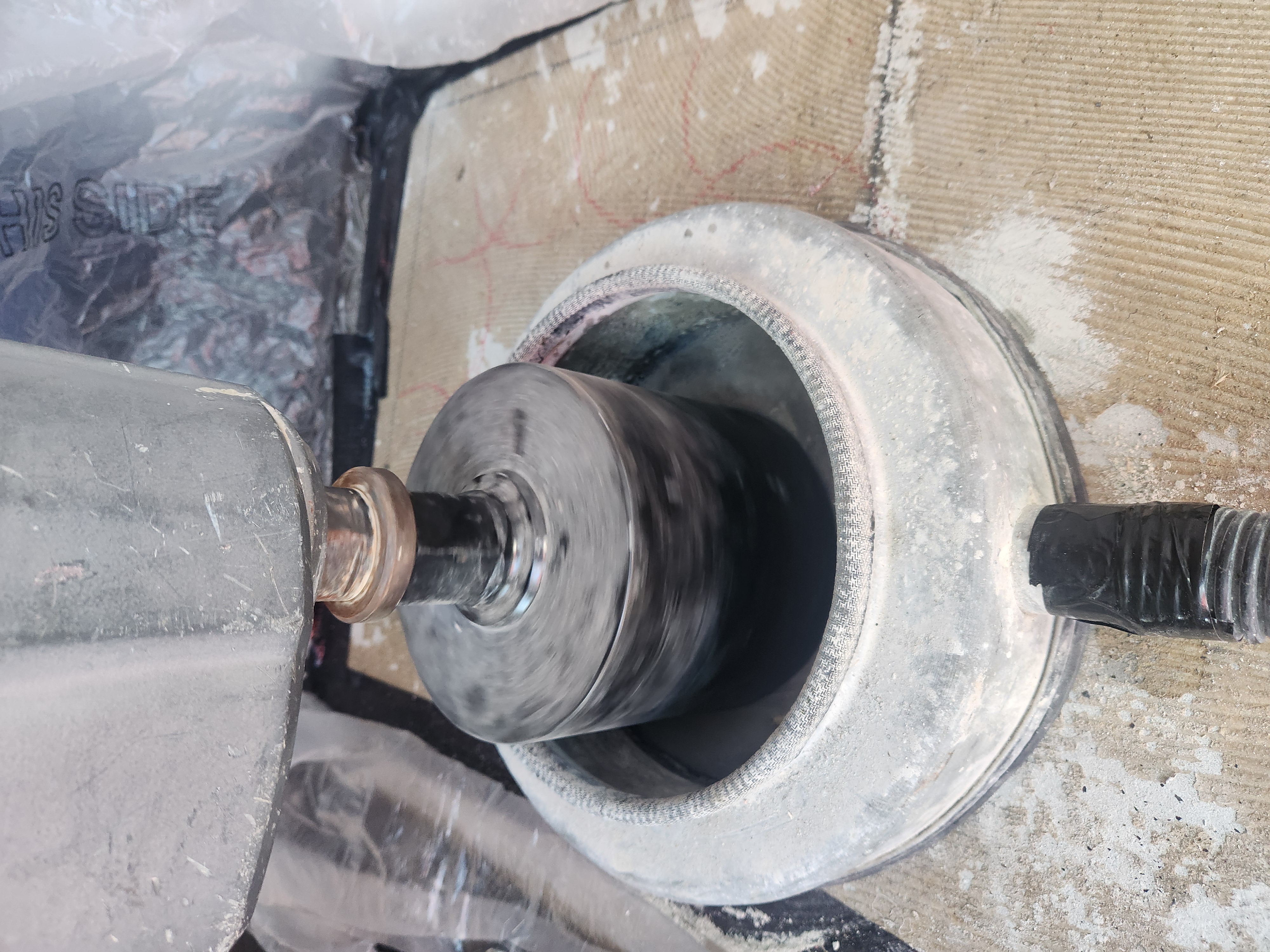Close-up of a rotating concrete coring drill bit inside a core barrel on a dusty surface.
