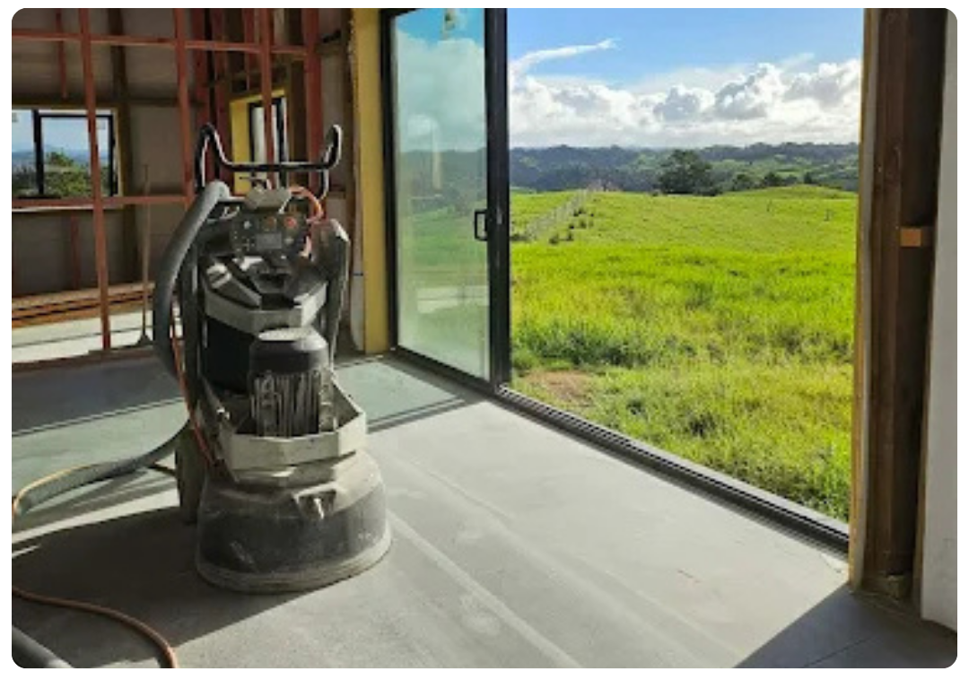 Concrete floor polishing machine inside a room with sliding glass door showing green field outside.