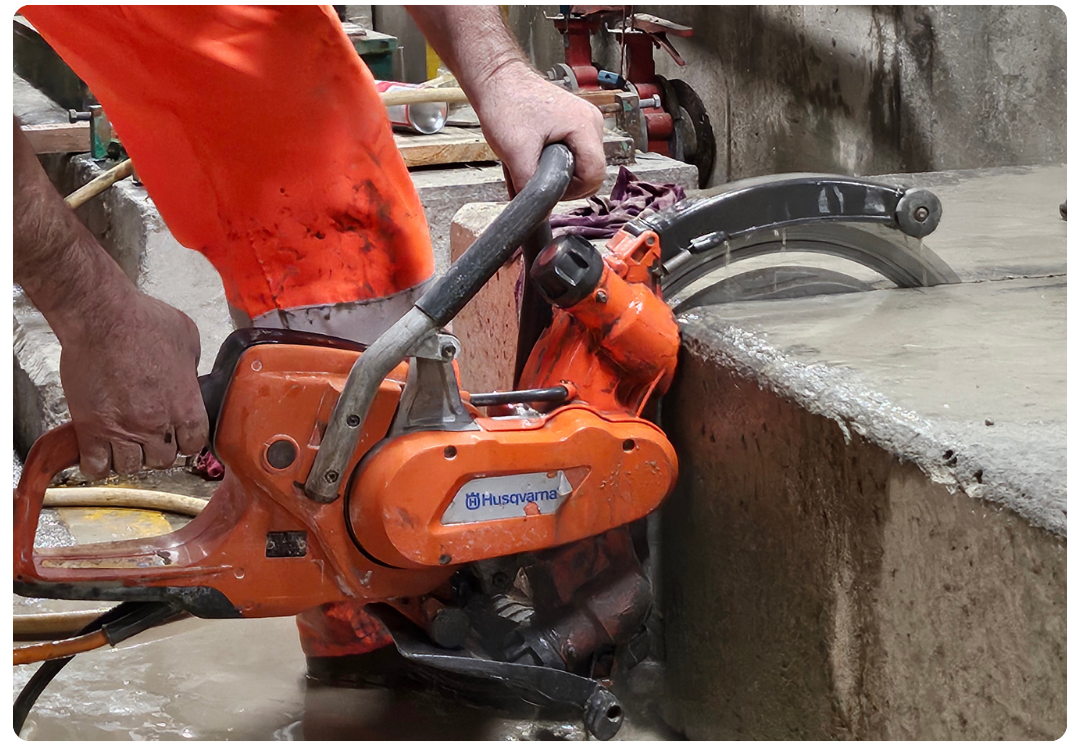 Worker using an orange Husqvarna concrete saw to cut a slab of concrete.