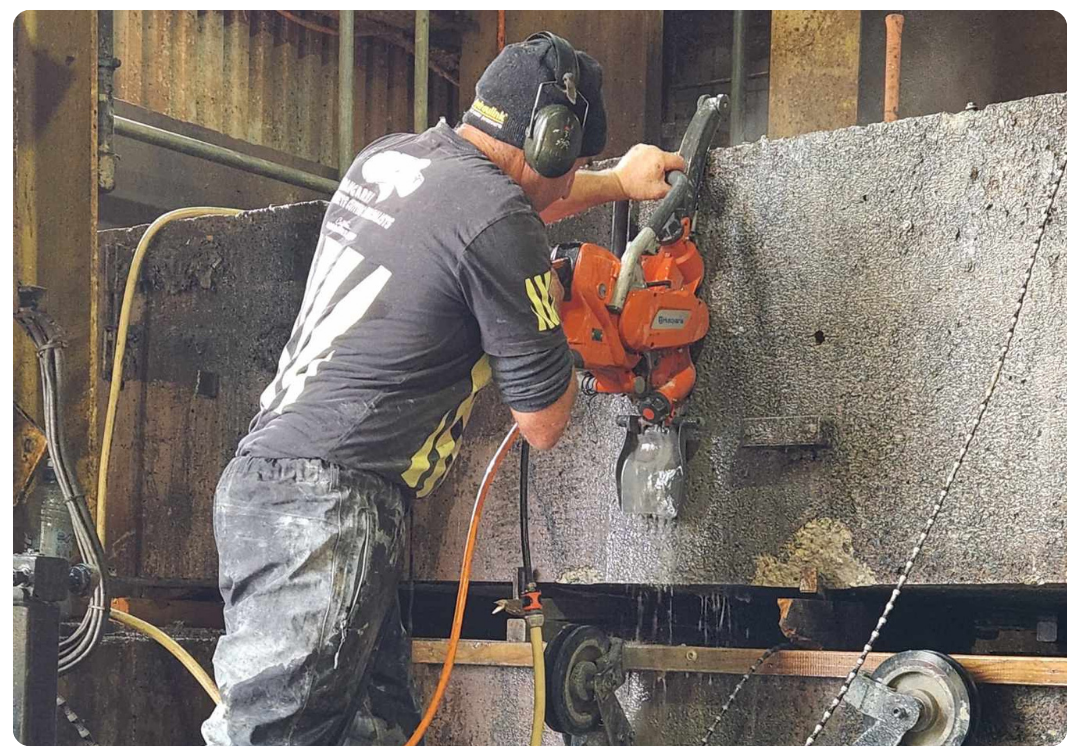 Worker using an orange Husqvarna power saw to cut a large concrete block in an industrial setting.