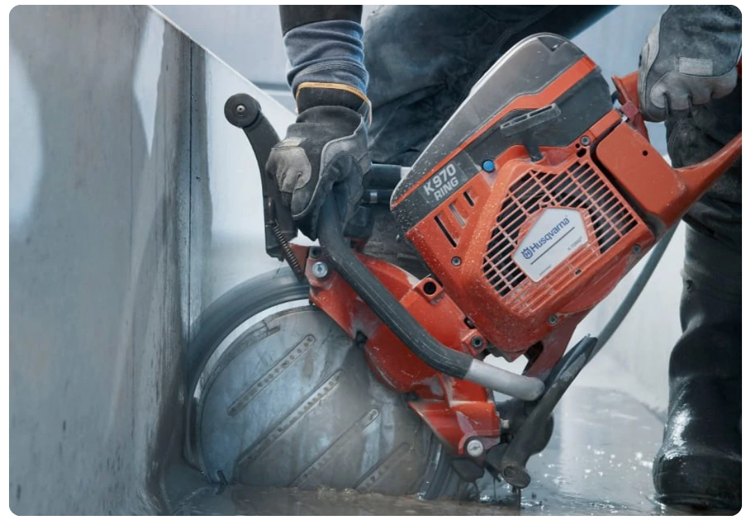 Gloved hands operating a Husqvarna K970 Ring saw to cut a concrete wall.