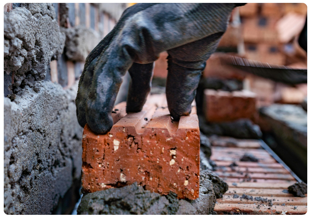 Gloved hand placing a brick on mortar during bricklaying.