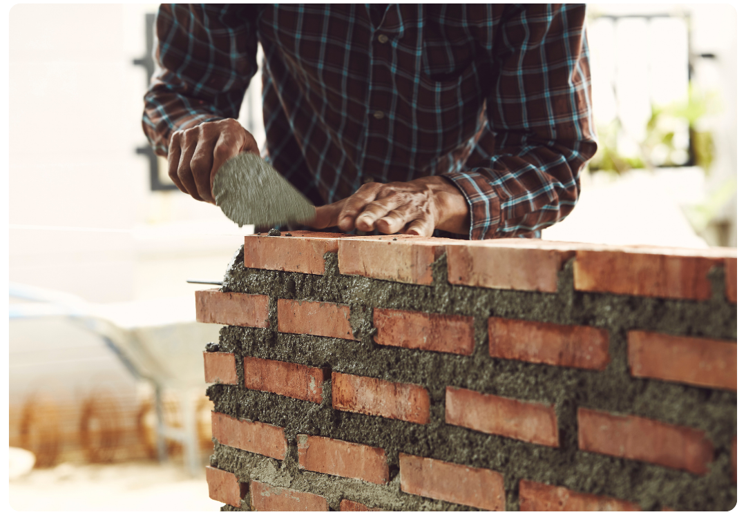Worker using a trowel to smooth mortar on a brick wall under construction.