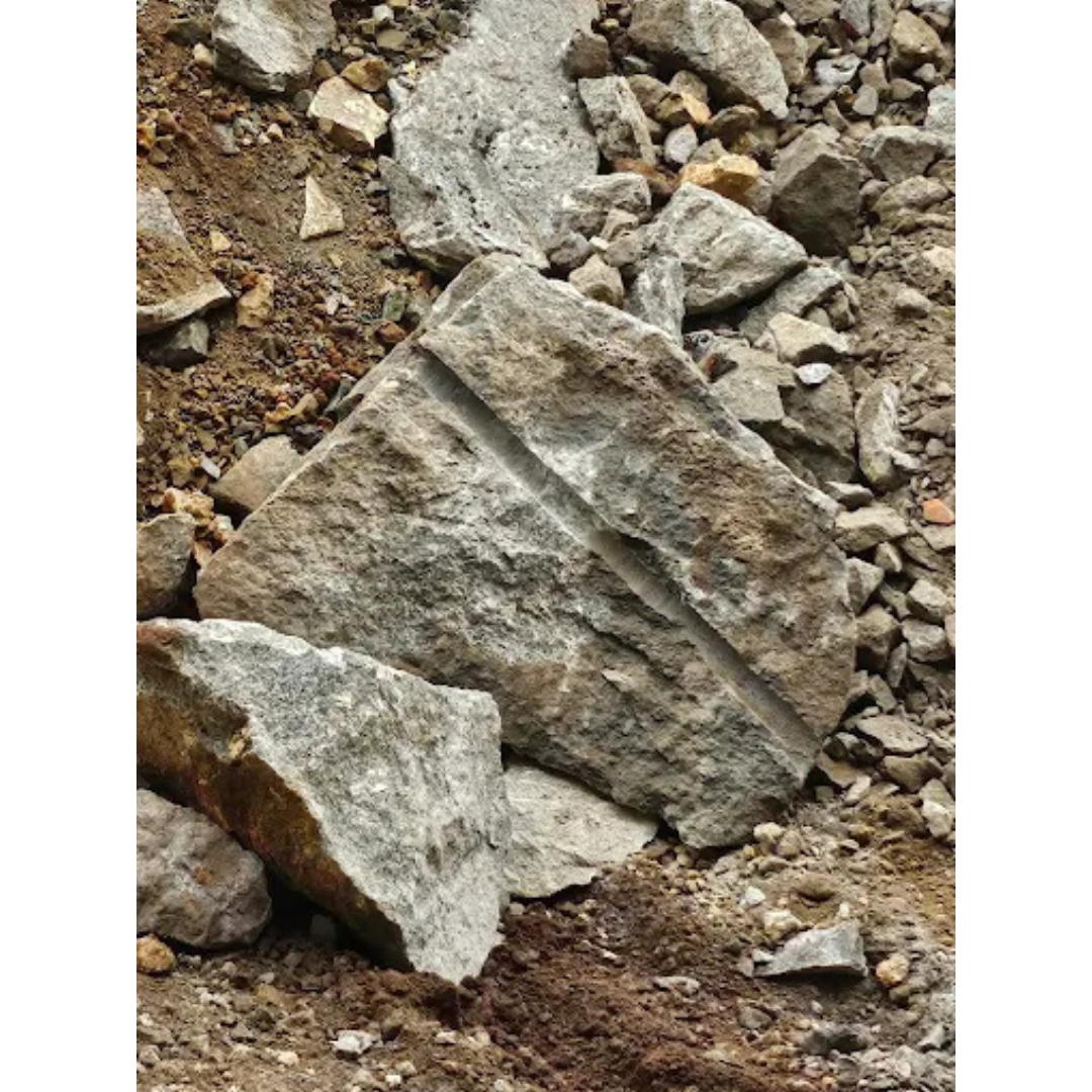 Close-up of large, broken gray rocks and smaller gravel on dry dirt ground.