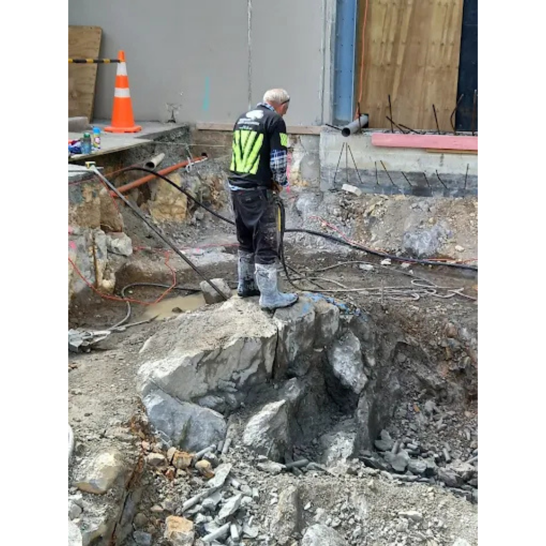 Construction worker using jackhammer on rocky ground at an excavation site.