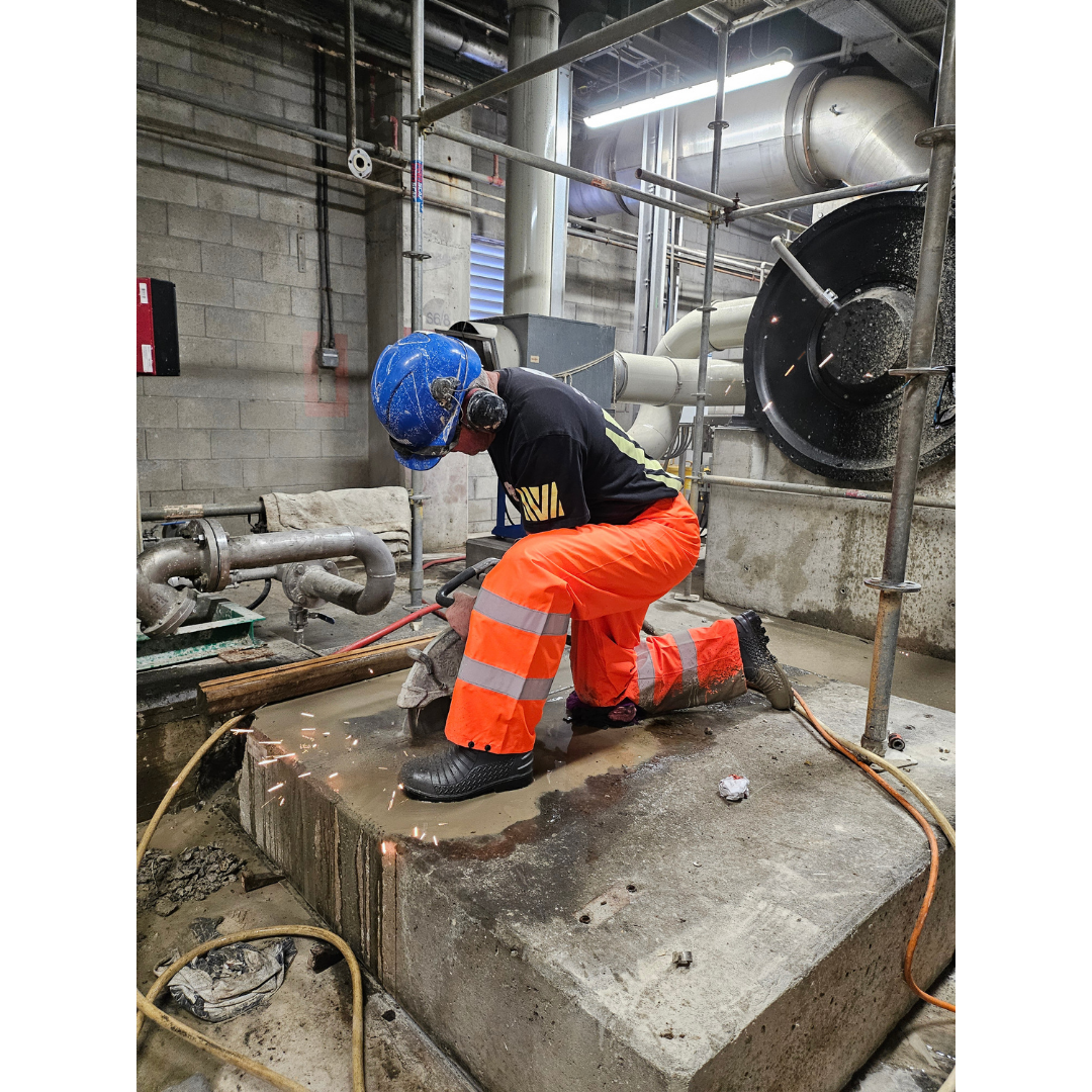 Worker in safety gear using a power saw to cut concrete inside an industrial facility.