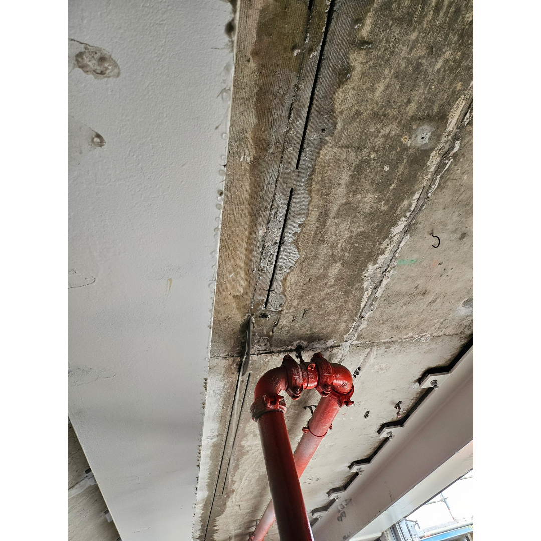 Red industrial pipes attached to a concrete ceiling in a building under construction.