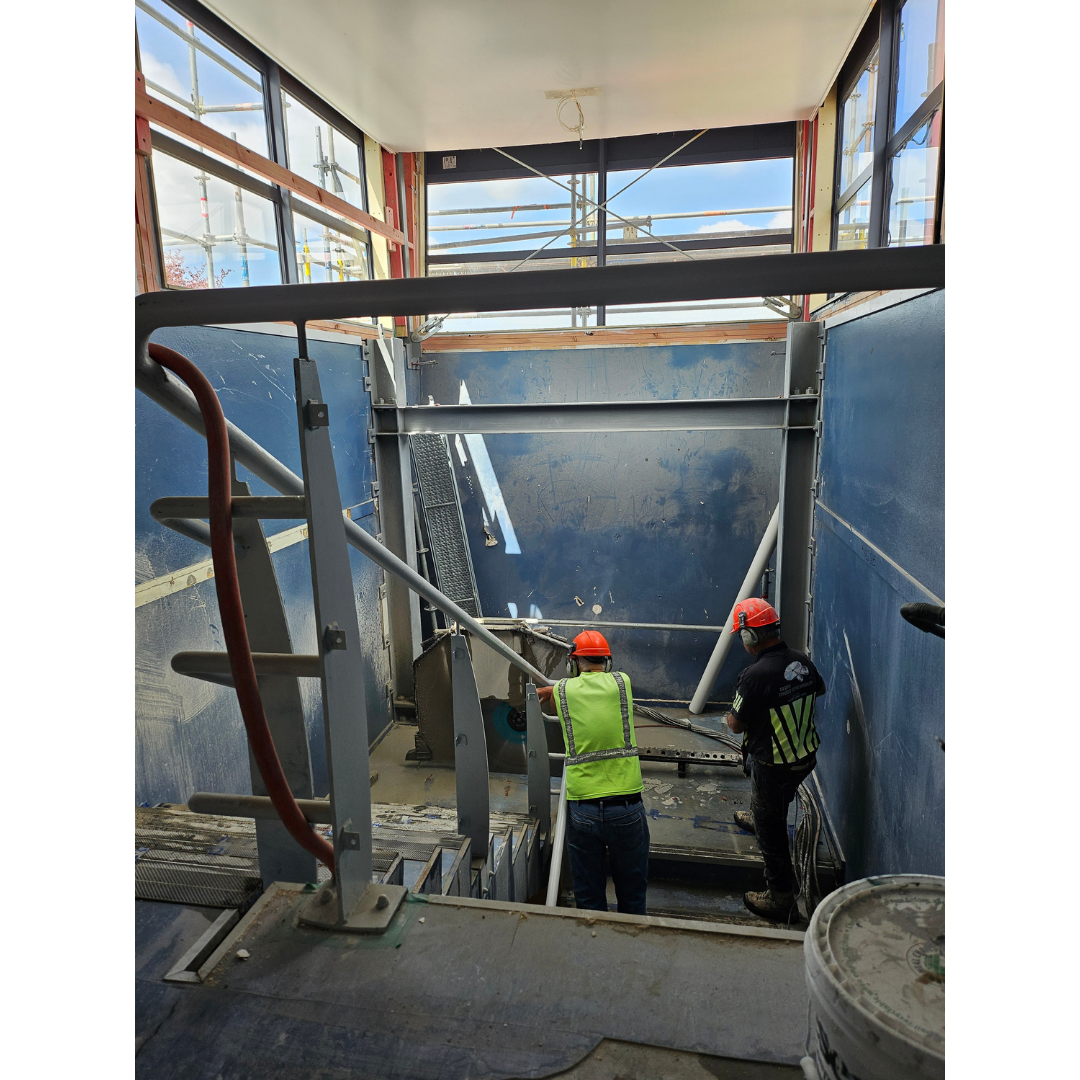 Two construction workers wearing helmets and safety vests working in a stairwell under construction.
