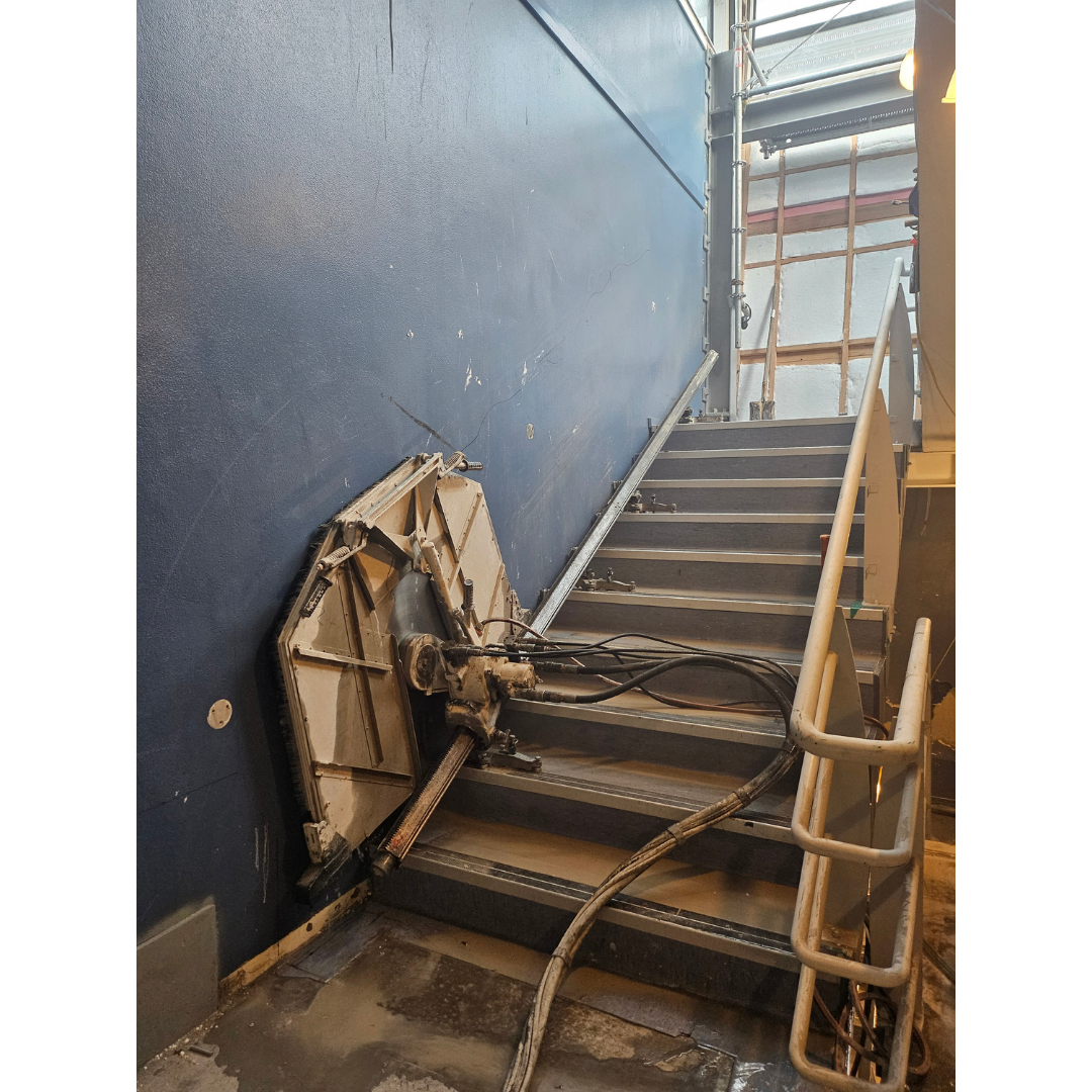 Metal staircase with a hydraulic lift mechanism attached to the wall beside the stairs.
